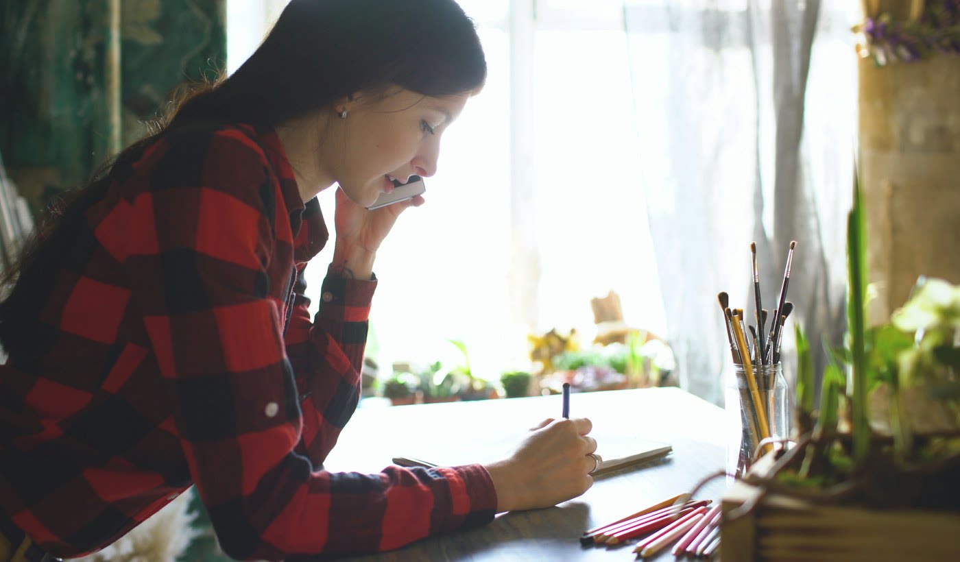 A woman on a phone call sketching notes in a notebook as she listens