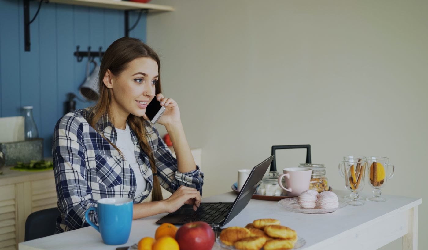 A woman on a phone call at her laptop in a home kitchen