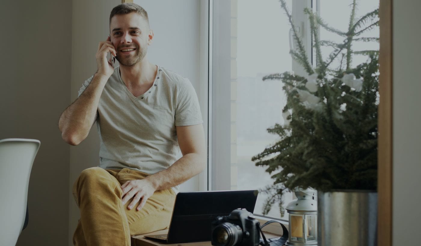 A man smiling on a phone call by a window in his home office