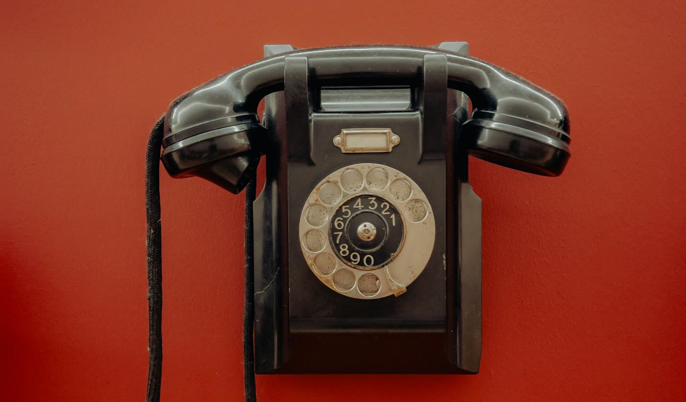 An old black telephone hanging on a red wall with nobody picking up