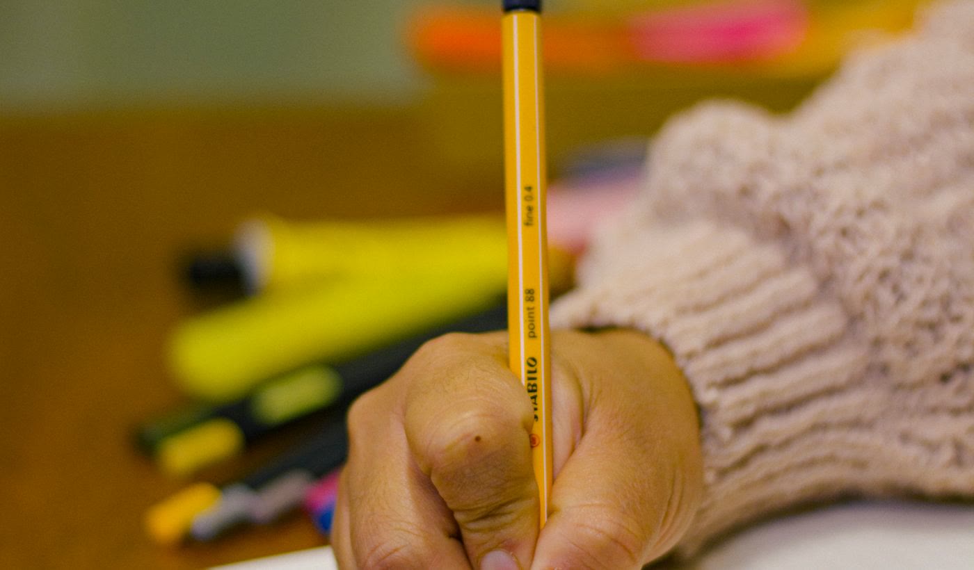 A hand writing lines in a notebook with a yellow pencil