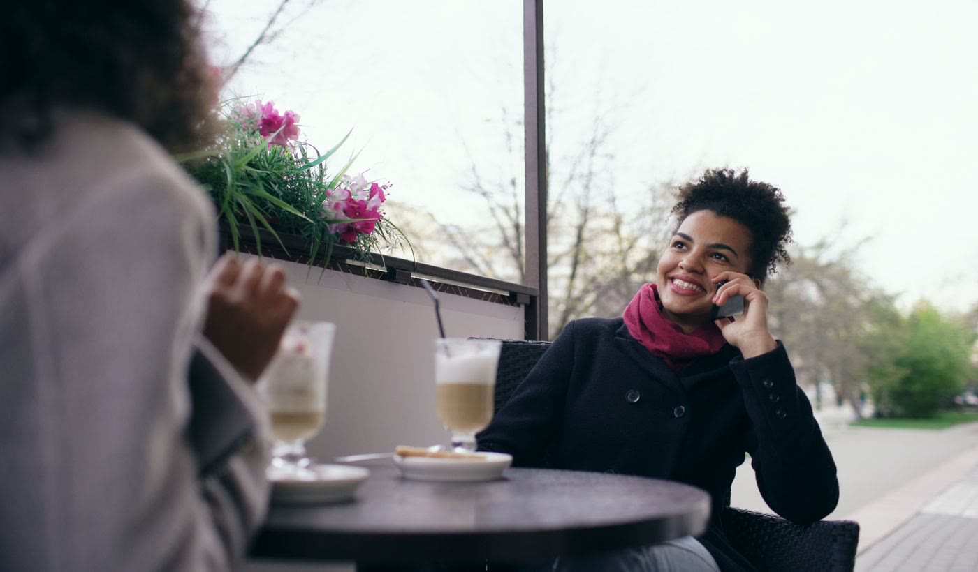 A woman smiling on a phone call at an outdoor cafe table