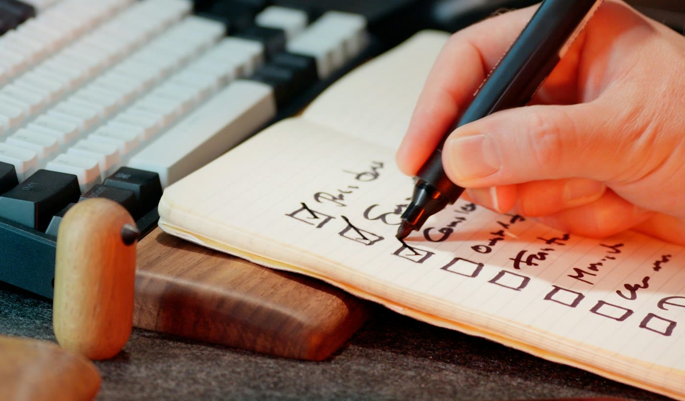 A hand ticking boxes on a handwritten checklist next to a keyboard