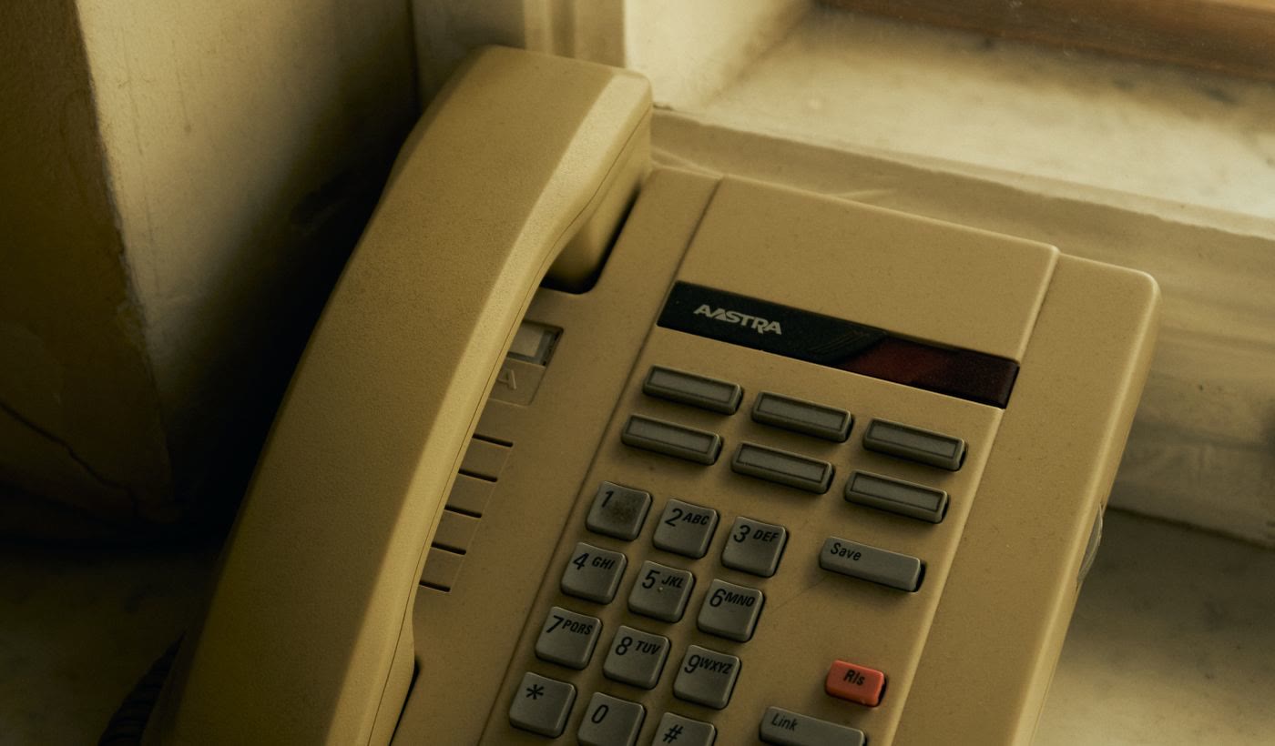 A beige office desk phone with a keypad on a sunlit desk