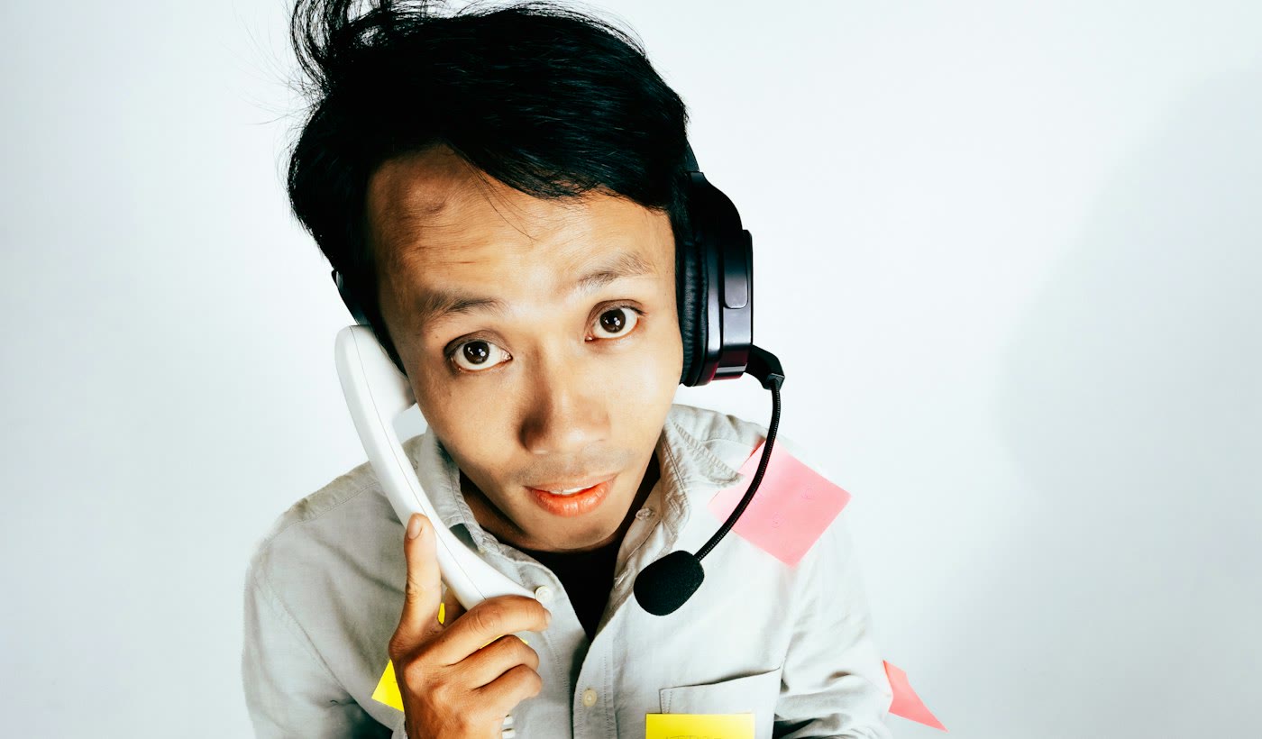 A man in a headset holding a desk phone and a radio at once, surrounded by sticky notes