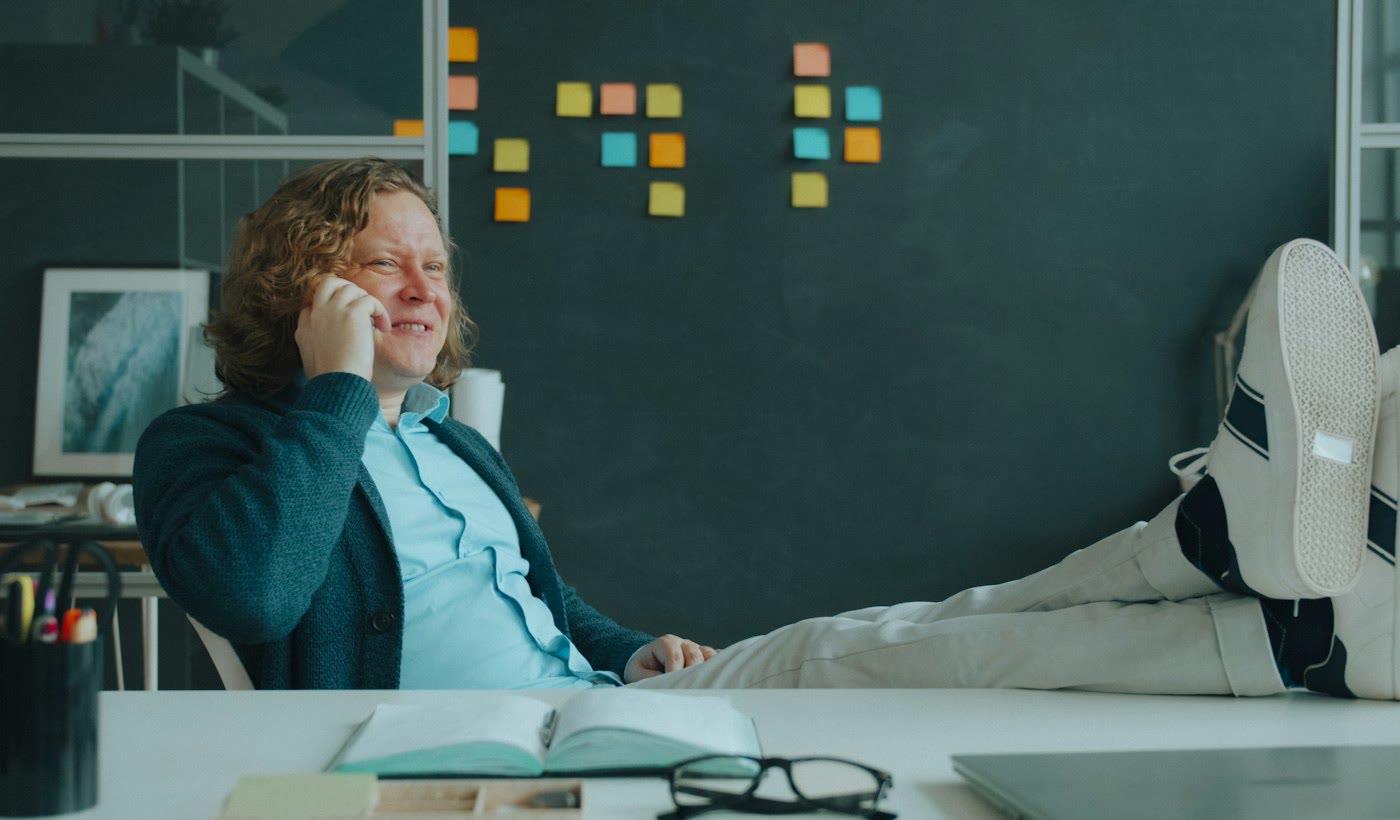 A man leaning back with his feet up, laughing on a phone call