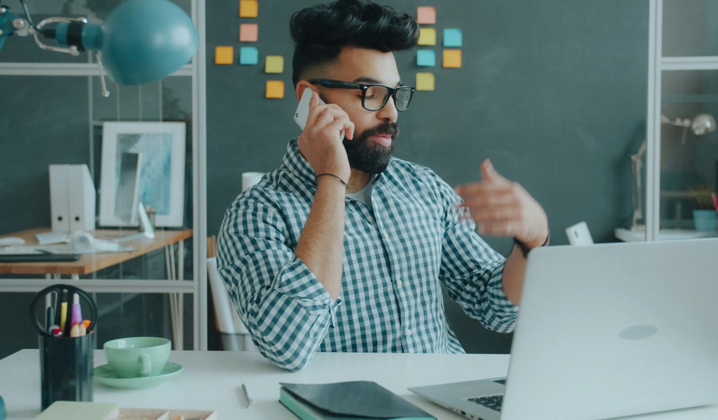 A man on a mobile phone call at his desk, gesturing as he talks