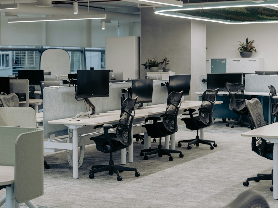 An empty open-plan office with rows of desks and monitors