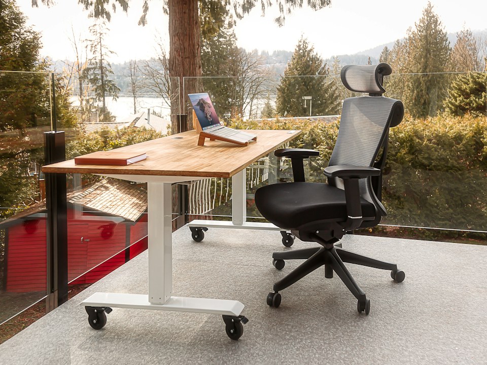 A standing desk and an office chair on a balcony above a lake