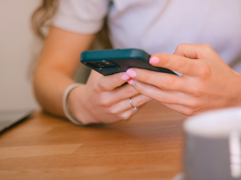 A person typing on a phone at a table