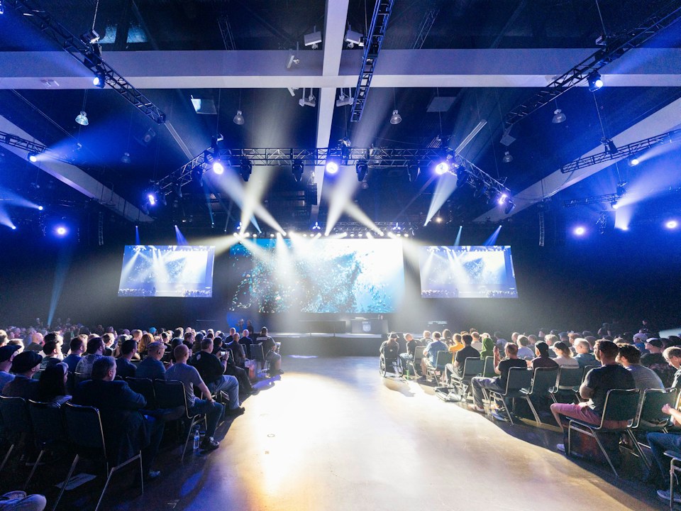 A large audience in front of a lit conference stage