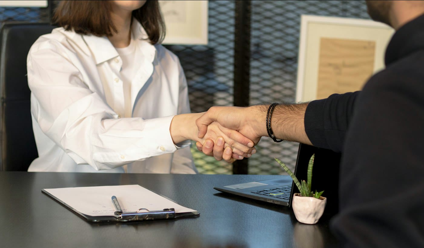 Two people shaking hands across a desk after a meeting
