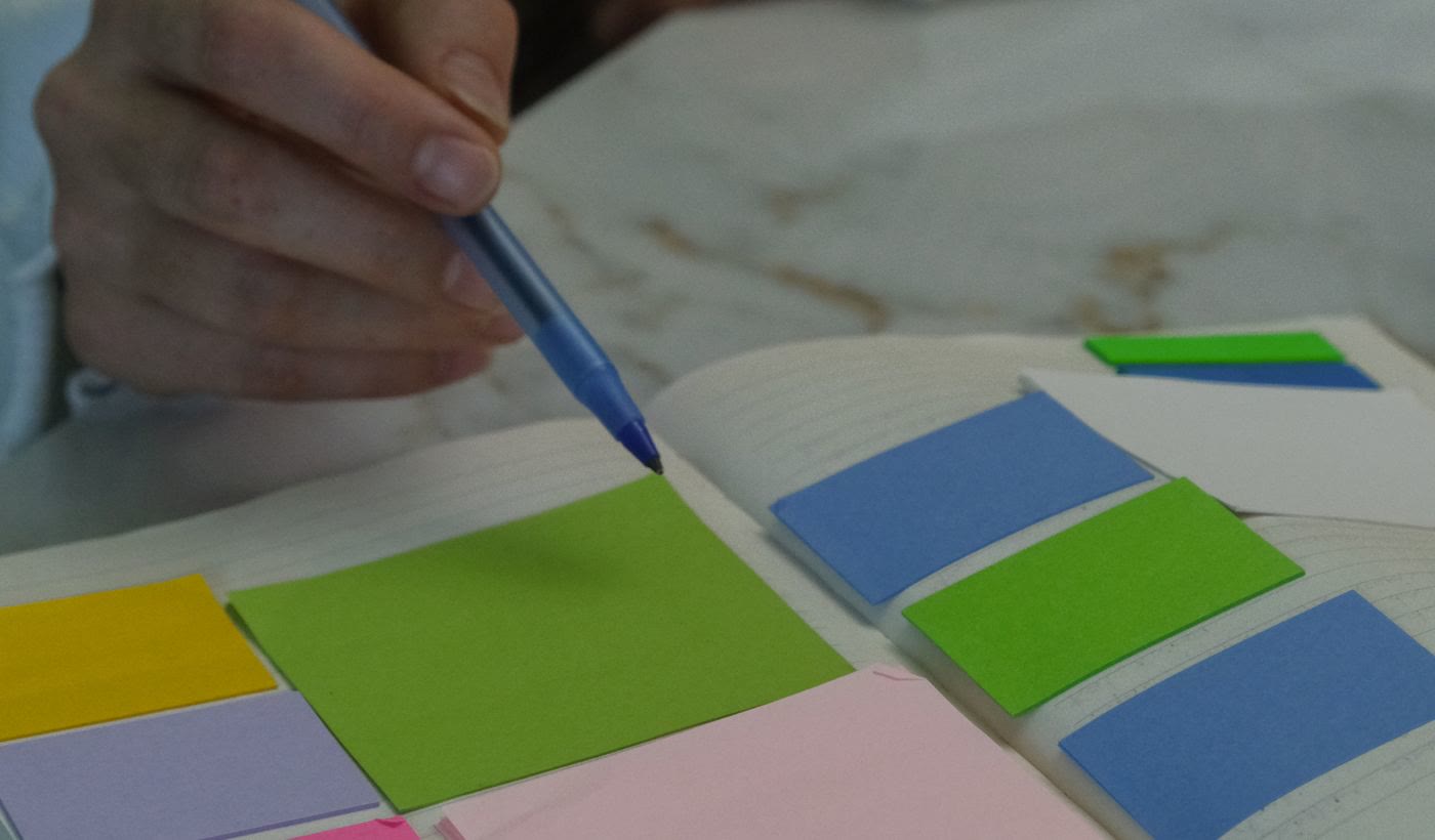 A pen pointing at coloured sticky notes laid out on a notebook