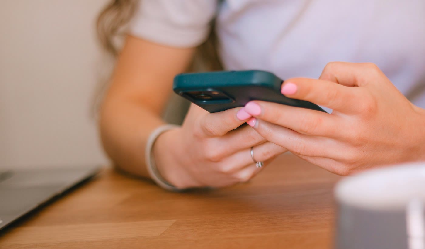 Two hands typing a message on a smartphone at a table